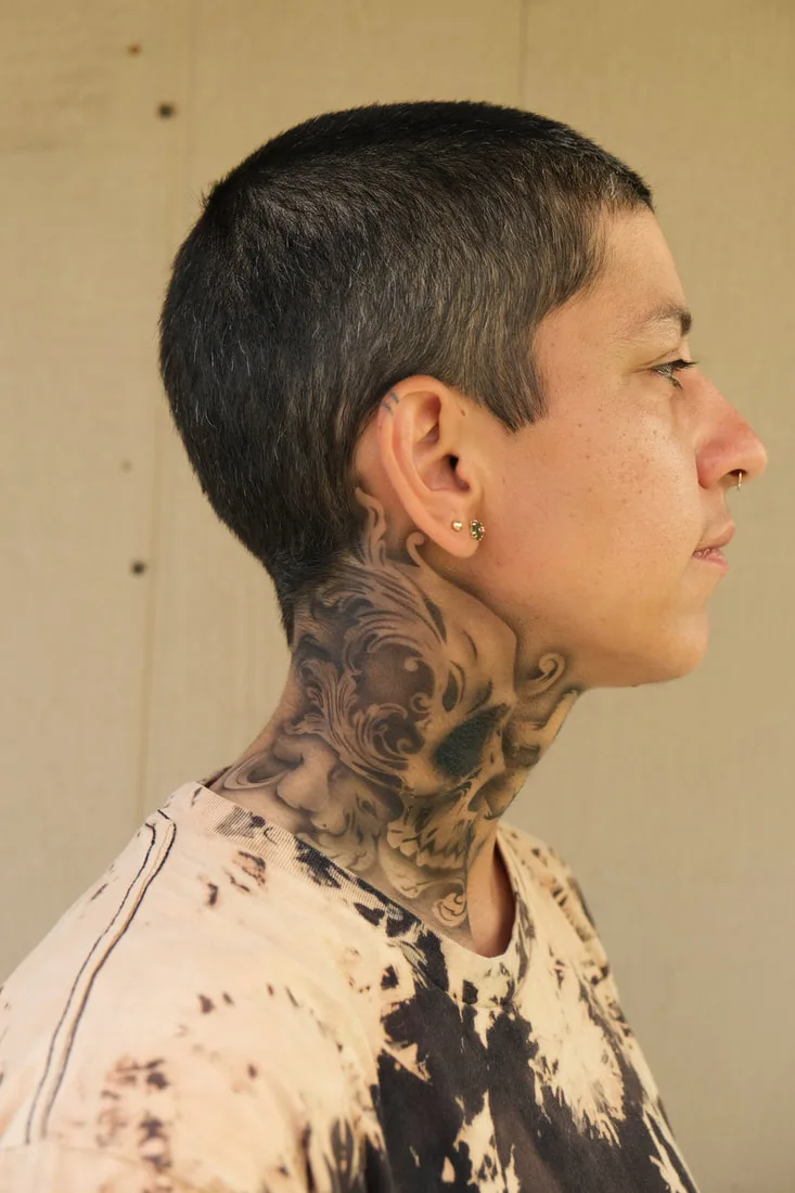 A person with a medium skin tone models a realistic airbrush tattoo of a skull and bones on their neck